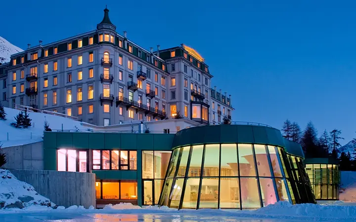 Un grande albergo di montagna di notte, nella neve, con un padiglione di vetro illuminato.