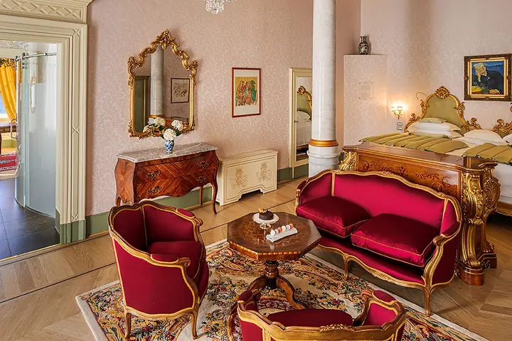 Una suite di Villa Serbelloni con i divani rossi, gli specchi dorati e il letto.